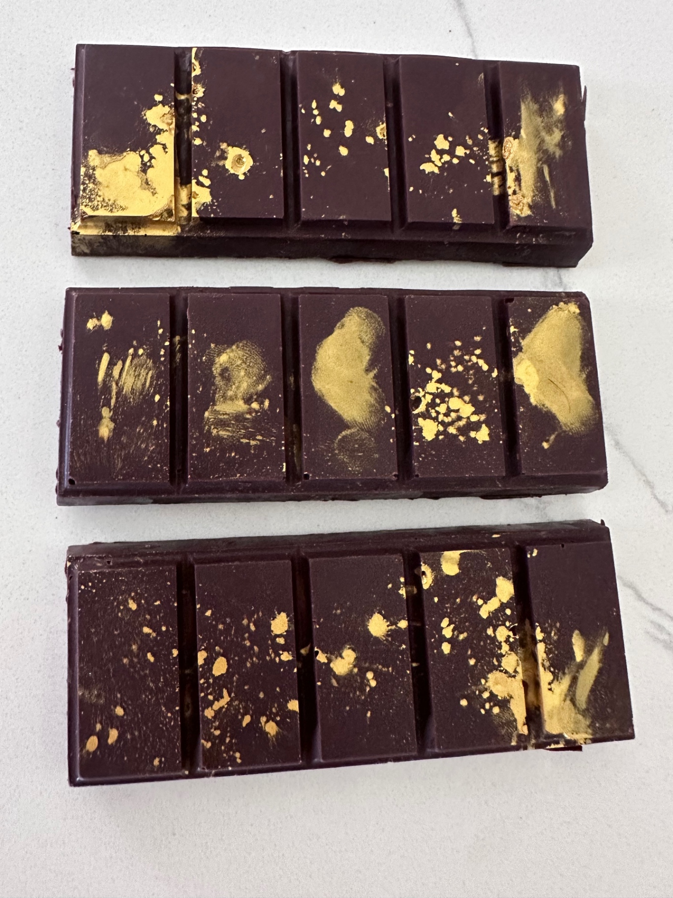 Three gold dusted Dubai chocolate bars on marble